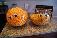 two glass bowls filled with candy corn and eyes on top of a granite countertop