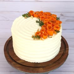 a cake with white frosting and orange flowers on top is sitting on a wooden platter