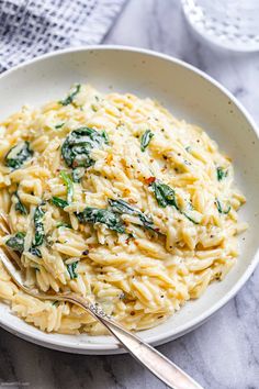 a white bowl filled with pasta and spinach on top of a marble countertop