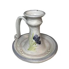 a white ceramic candle holder with blue flowers on the front and green leaves on the outside