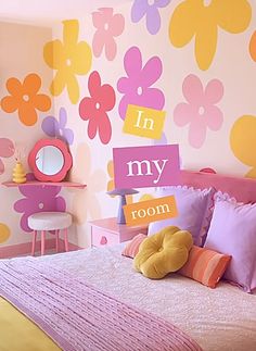 a child's bedroom decorated in pink, yellow and purple with flowers on the wall