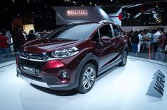 a red car is on display at an auto show with people looking around the vehicle