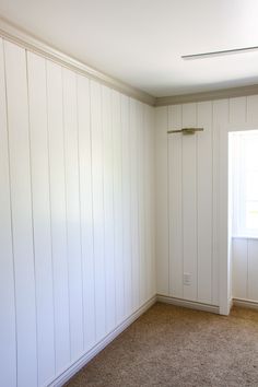 an empty room with white paneling and a window in the corner on the far wall