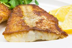 two pieces of fish on a white plate with lemon wedges and spinach leaves