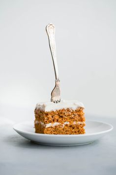 a piece of carrot cake on a white plate with a fork stuck in the top