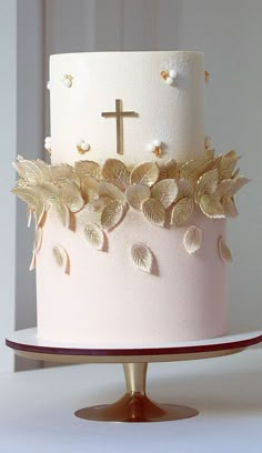 a white cake with gold leaves and a cross on top is sitting on a plate