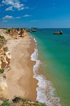 a sandy beach next to the ocean under a blue sky