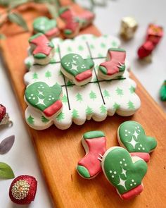 decorated cookies sitting on top of a wooden cutting board next to strawberries and leaves