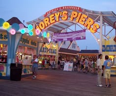 an amusement park with lots of rides and people on the boardwalk at night time,