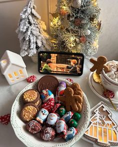 a white plate topped with lots of cookies next to a christmas tree and cell phone