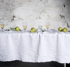 two glasses and three pears on a table with white linen draped over it, in front of a stone wall