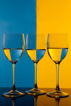 three wine glasses sitting next to each other on top of a wooden table in front of a blue and yellow wall