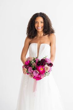 a woman in a wedding dress holding a bouquet of flowers and smiling at the camera