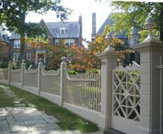 a white picket fence in front of a house with trees and bushes on the side