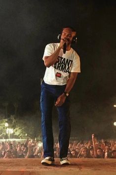 a man standing on top of a stage holding a microphone to his ear while singing