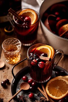 two glasses of mulled with orange slices and cranberries on a plate next to an ice bucket