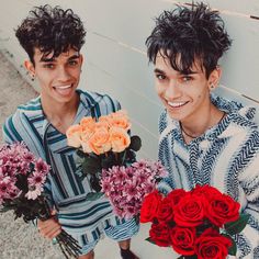 two young men holding bouquets of roses and smiling at the camera while standing next to a wall