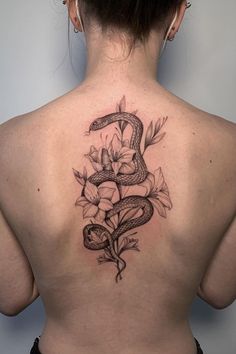 a woman's back with a snake and flowers tattoo on her left side ribcage