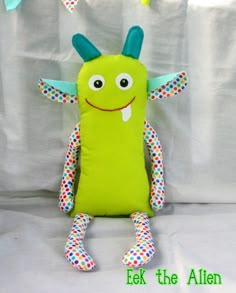 a green stuffed animal with polka dots on it's arms and legs sitting in front of a white background