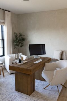 a desk with a computer on it in front of a couch and chair next to a window