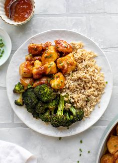 a white plate topped with chicken and broccoli covered in sauce next to other dishes