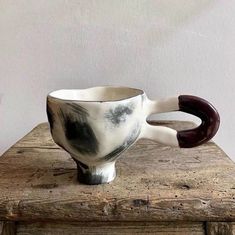 a white and black ceramic cup sitting on top of a wooden table next to a wall