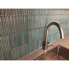 a stainless steel sink and faucet against a green glass tile backsplash