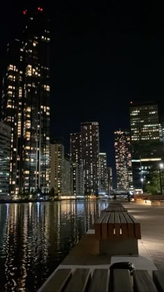 a bench sitting on the side of a river next to a tall building at night