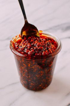 a spoon in a jar filled with food on top of a white countertop next to a marble surface