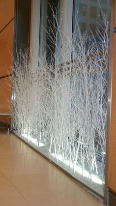 a cat sitting on the floor in front of a window with white branches behind it