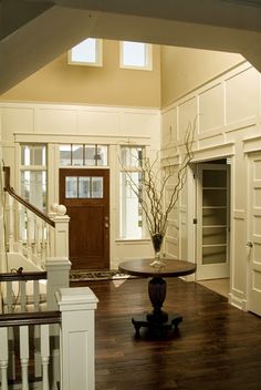 an entry way with white walls and wood flooring in the center is flanked by a wooden staircase that leads to another room