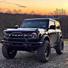 a black truck parked on top of a gravel road next to a forest at sunset