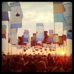 a crowd of people standing next to each other with flags flying in the air at sunset