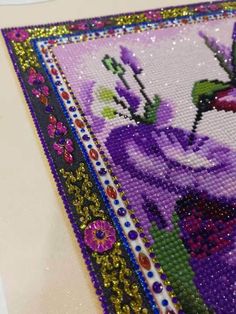 there is a beaded picture on the table with purple flowers and butterflies in it