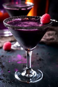 two martini glasses filled with purple liquid and raspberries on the rim, sitting next to each other