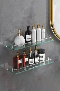 three glass shelves with bottles and soaps on them in front of a wall mirror