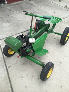 a green lawn mower sitting on top of a cement floor next to a building