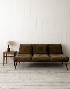 a brown couch sitting on top of a wooden floor next to a table and lamp