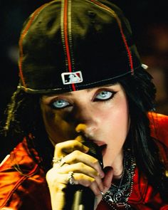 a woman with blue eyes and black hair holding a microphone up to her mouth while wearing a baseball cap