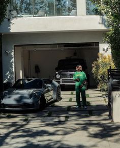 a man standing next to two cars in front of a house