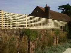 a brick wall and fence with grass growing on the side next to it in front of a house