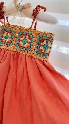 an orange dress with blue and brown flowers on the bottom is hanging from a rack