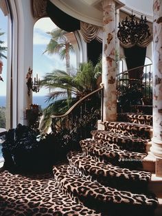 an ornate staircase with leopard print carpet and chandelier on the top floor next to palm trees