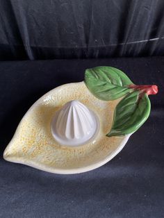 a white ceramic object with green leaves and a red flower on it's side