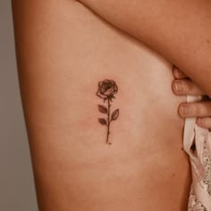 a woman's stomach with a rose tattoo on her left side ribcage