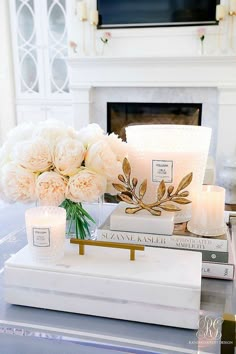 candles, flowers and books on a table in front of a fireplace