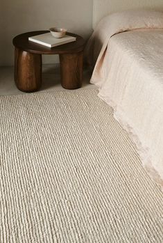 a white bed sitting next to a wooden table on top of a carpeted floor