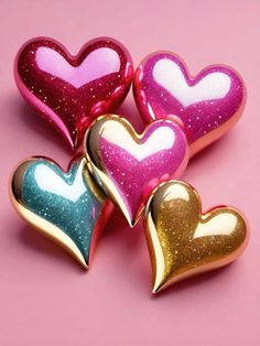 three heart shaped candy tins sitting on top of a pink surface with gold foil