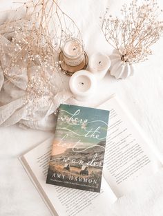 an open book sitting on top of a white blanket next to candles and some flowers