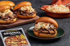 three pulled pork sandwiches on buns with coleslaw in the background and a cookbook